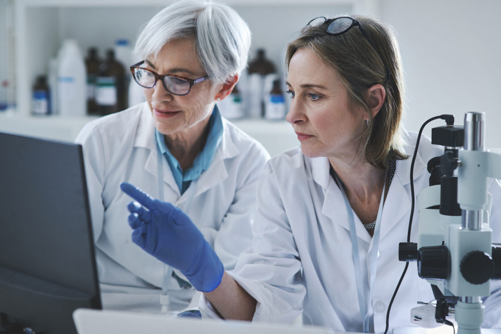 Two female scientists in lab coats examining a sample together.